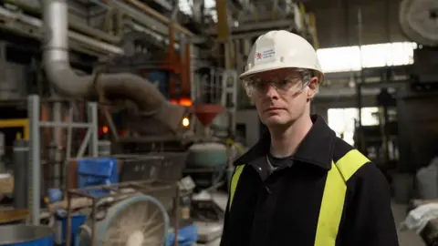 BBC News / Kevin Church Image of scientist, Dr Cyrille Dunant, standing in front of the electric arc furnace at the Materials Processing Laboratory in Middlesborough.  The furnace is glowing red hot.